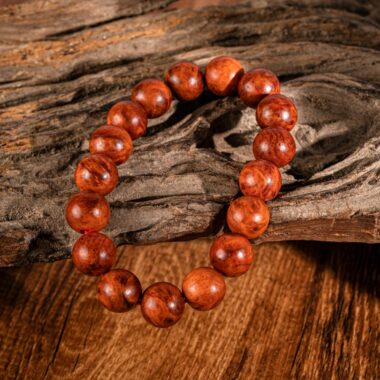 A close-up of a wooden beaded bracelet placed on textured driftwood, featuring warm tones.