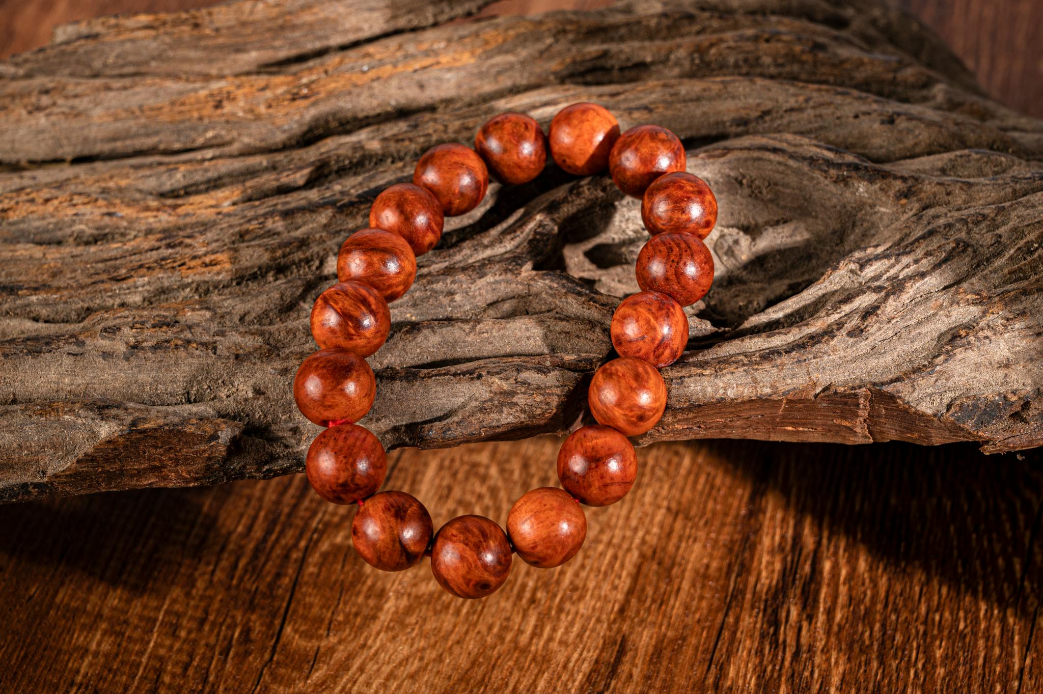 A close-up of a wooden beaded bracelet placed on textured driftwood, featuring warm tones.