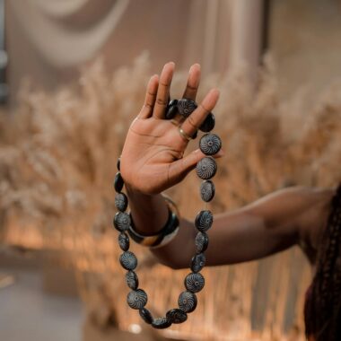 Close-up of a handcrafted beaded necklace held in a woman's hand against a rustic background.