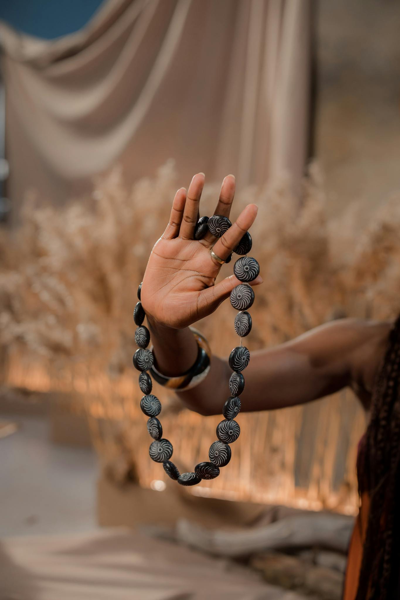 Close-up of a handcrafted beaded necklace held in a woman's hand against a rustic background.