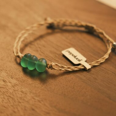 Close-up of a handcrafted bracelet with green glass beads on a wooden table.