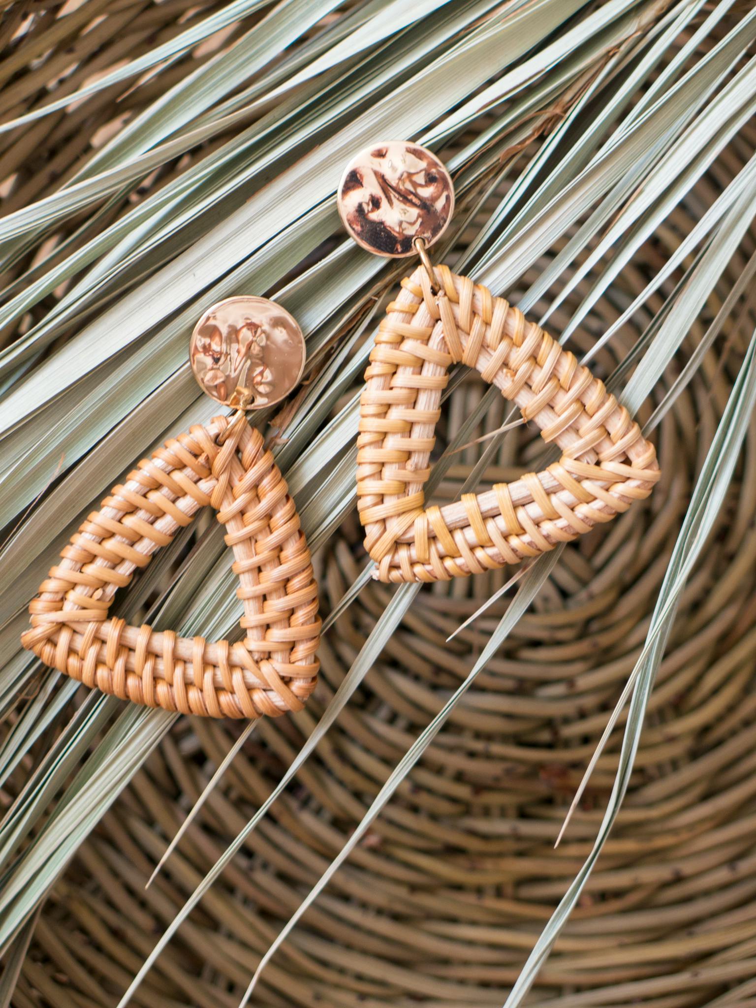 Close-up of triangular rattan earrings on woven straw backdrop, perfect for fashion and style themes.