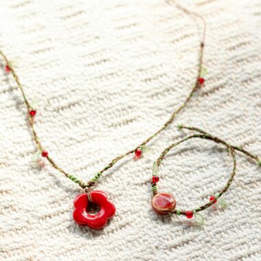 Elegant red flower pendant necklace and bracelet set on textured fabric.